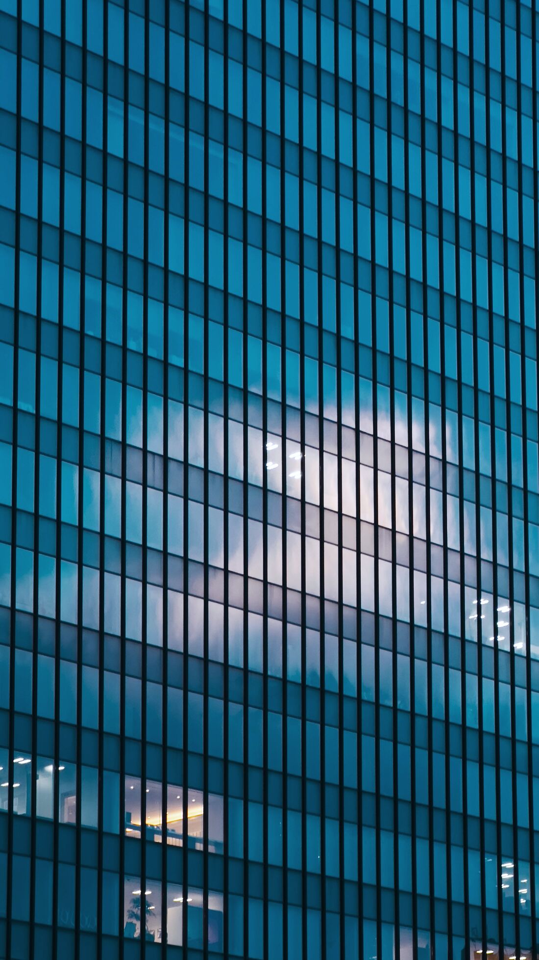 A glass curtain-wall office tower reflecting cloud at dusk.