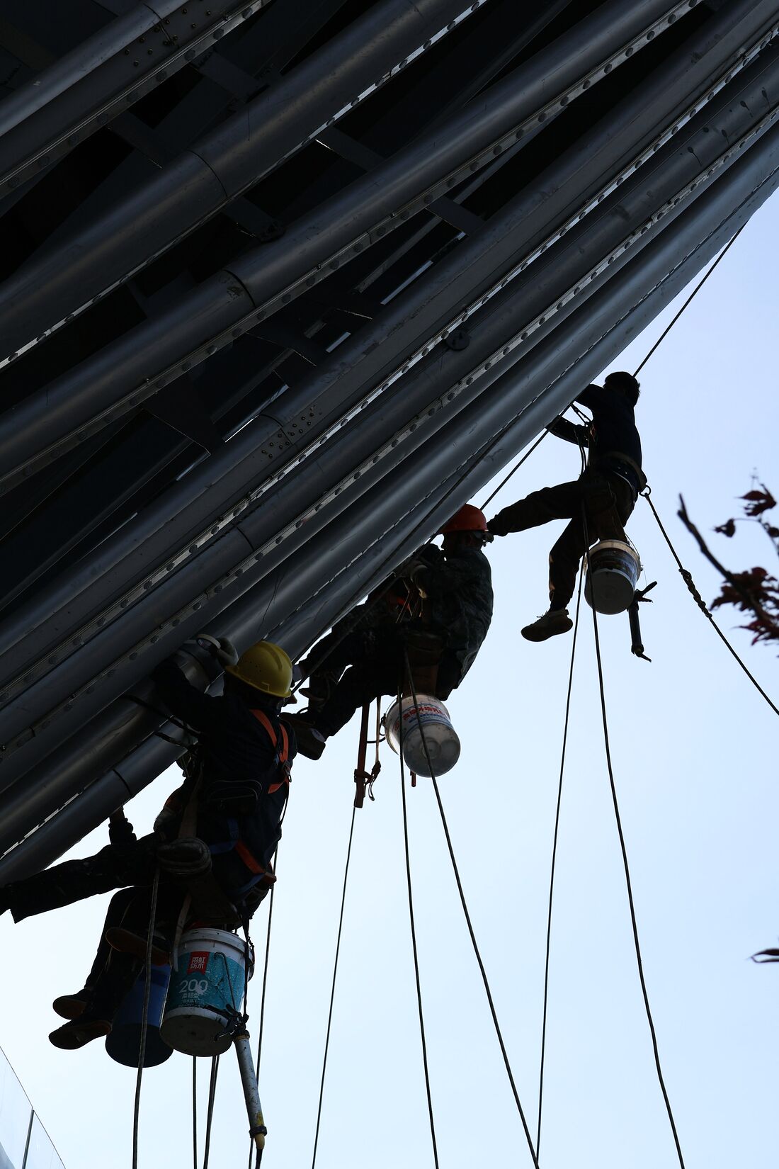 Two technicians suspended on ropes recoating the underside of a steel structure.