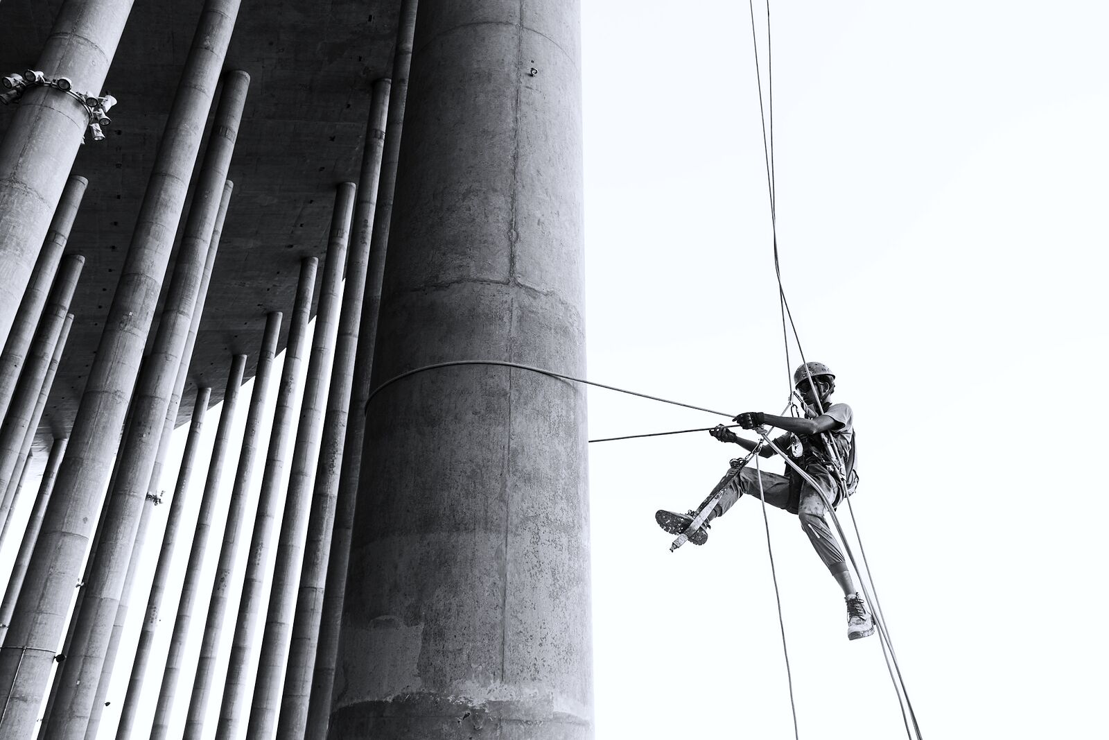 A technician rappelling down a tall concrete silo, photographed in black and white.