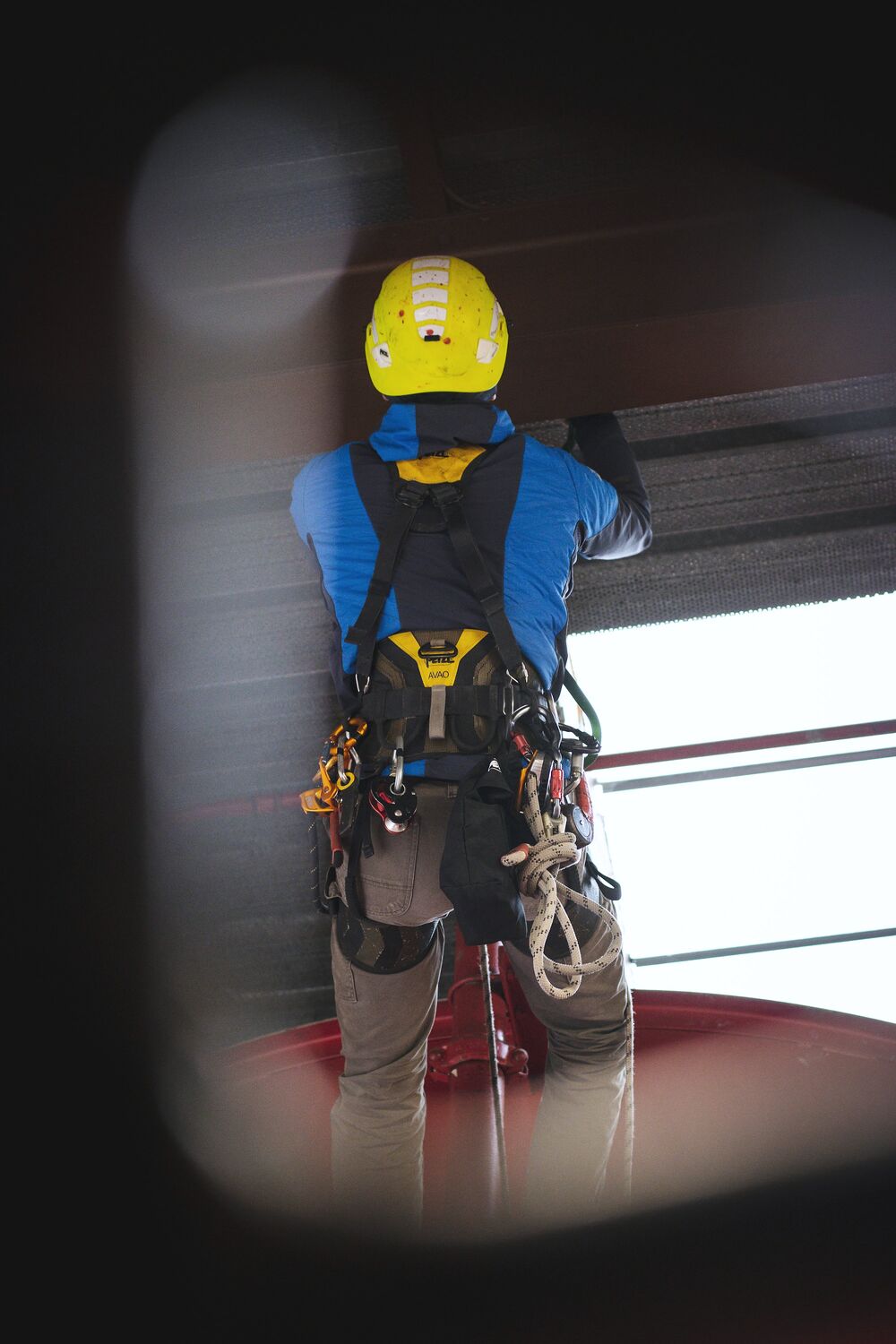 A rope access technician in a yellow helmet and full harness working at height.